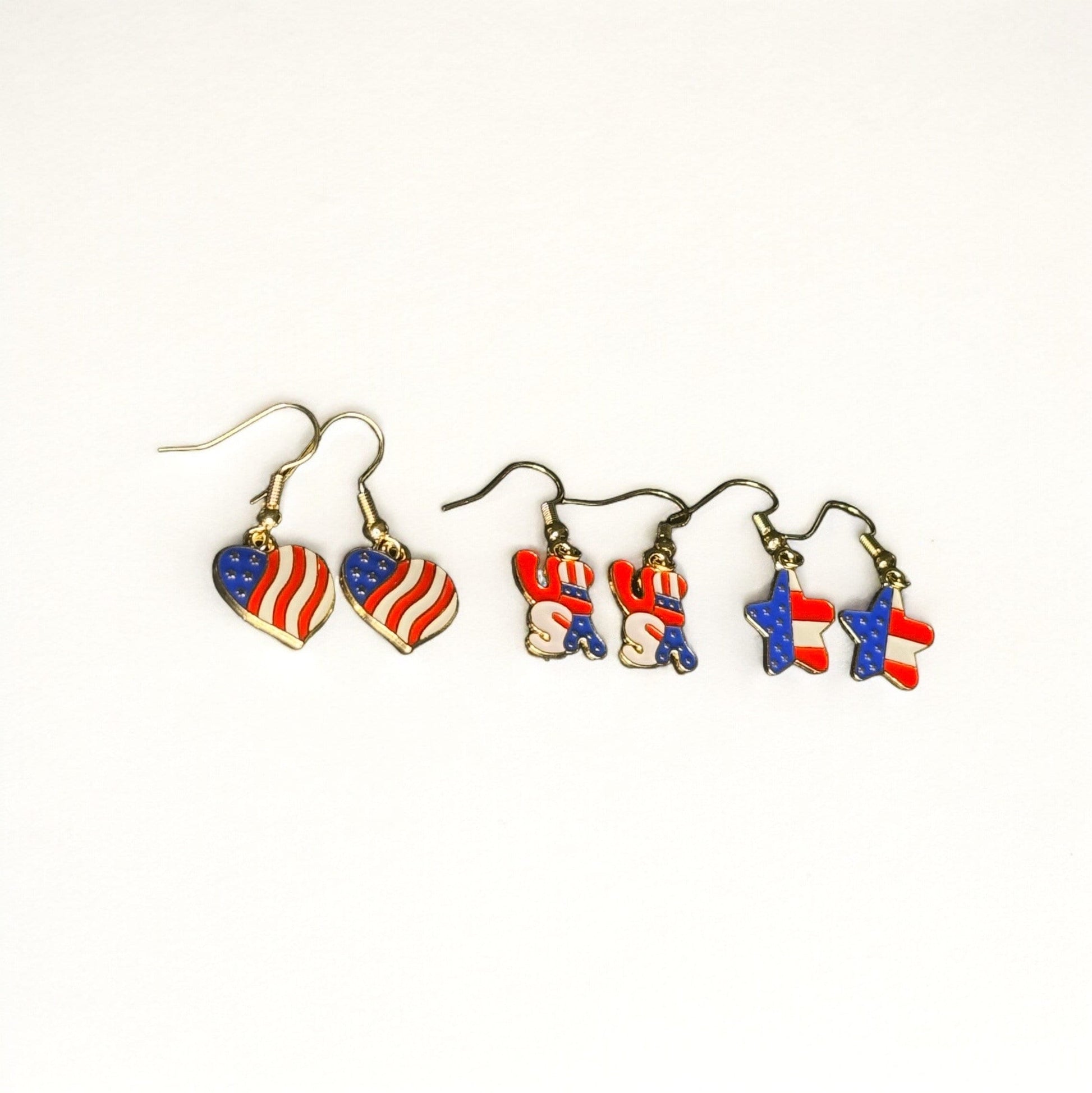 3 sets of 4th of July themed dangle earrings. All are printed like the U.S Flag. One is heart shaped, one is shaped in bubble letters spelling USA, and one is star shaped.