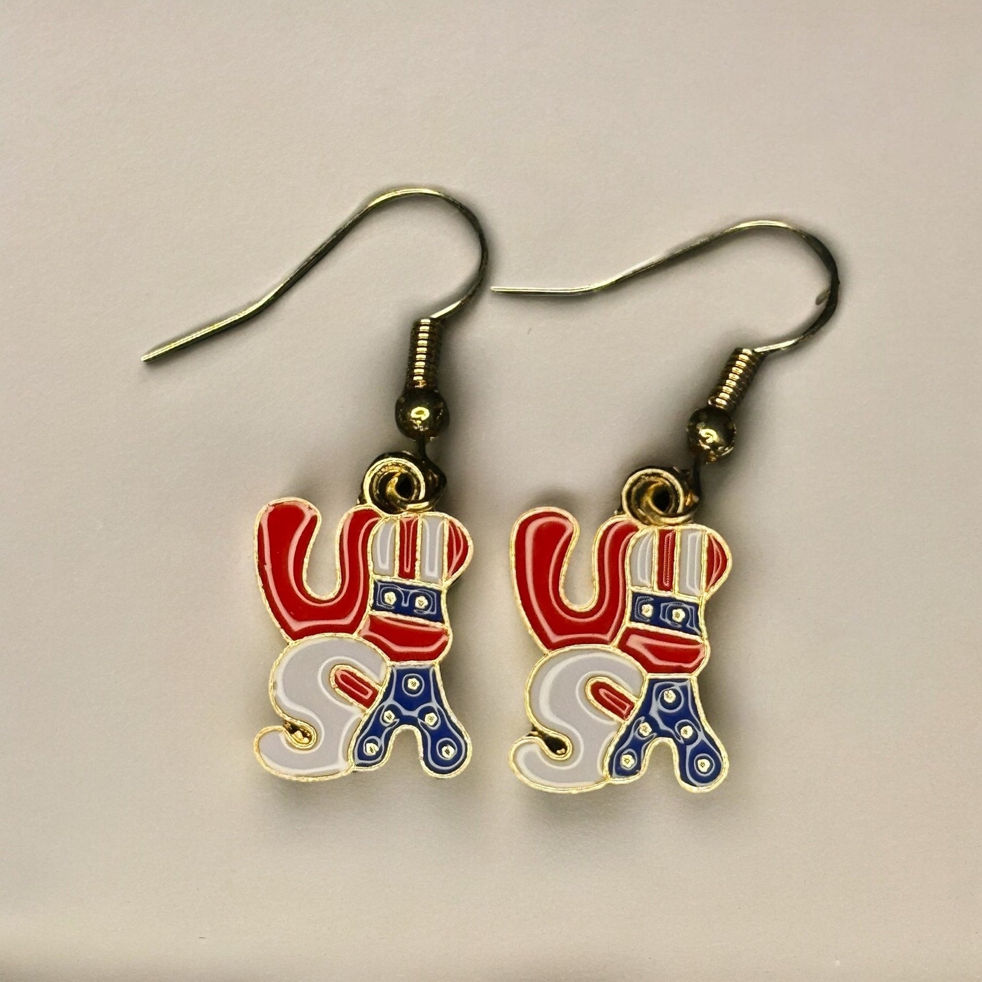 A pair of enamel dangle earrings colored red, white and blue like the USA flag spelling out in bubble letters "USA"