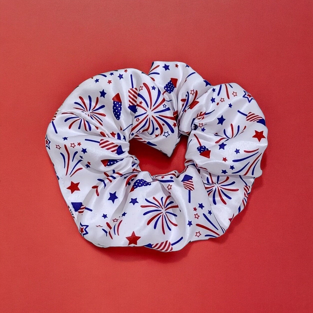 One scrunchie that is primarily white with red and blue fireworks and stars printed all over it.