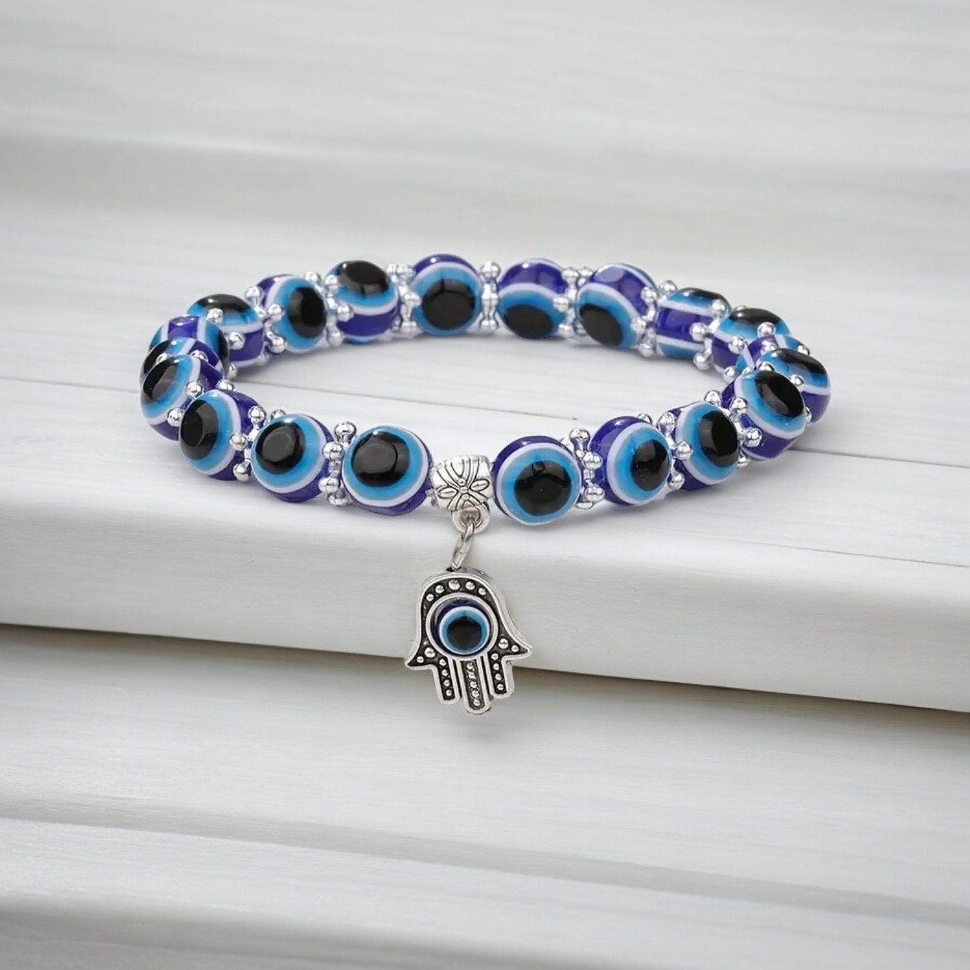 Blue beaded evil eye Hamsa hand bracelet laying on a white countertop.