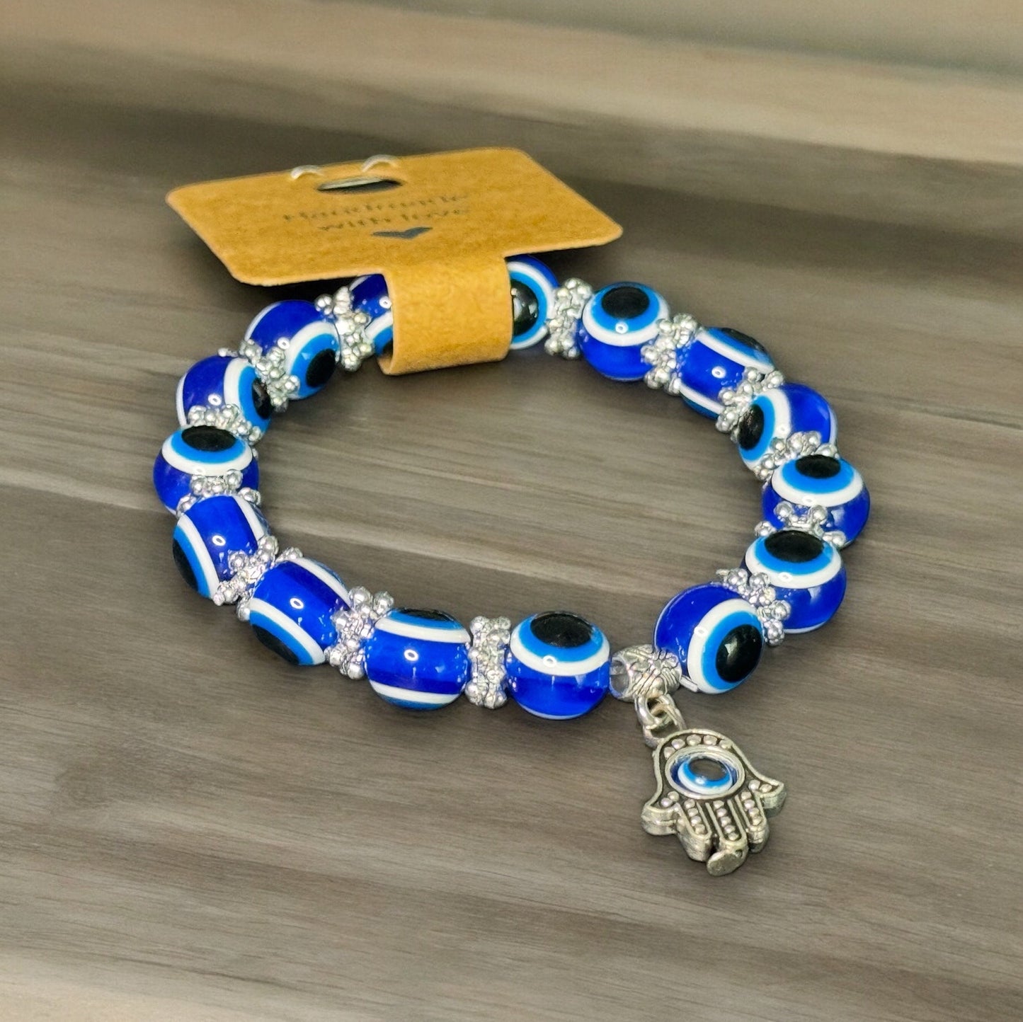 One blue beaded evil eye bracelet with hamsa hand charm laying sideways on a wooden surface.