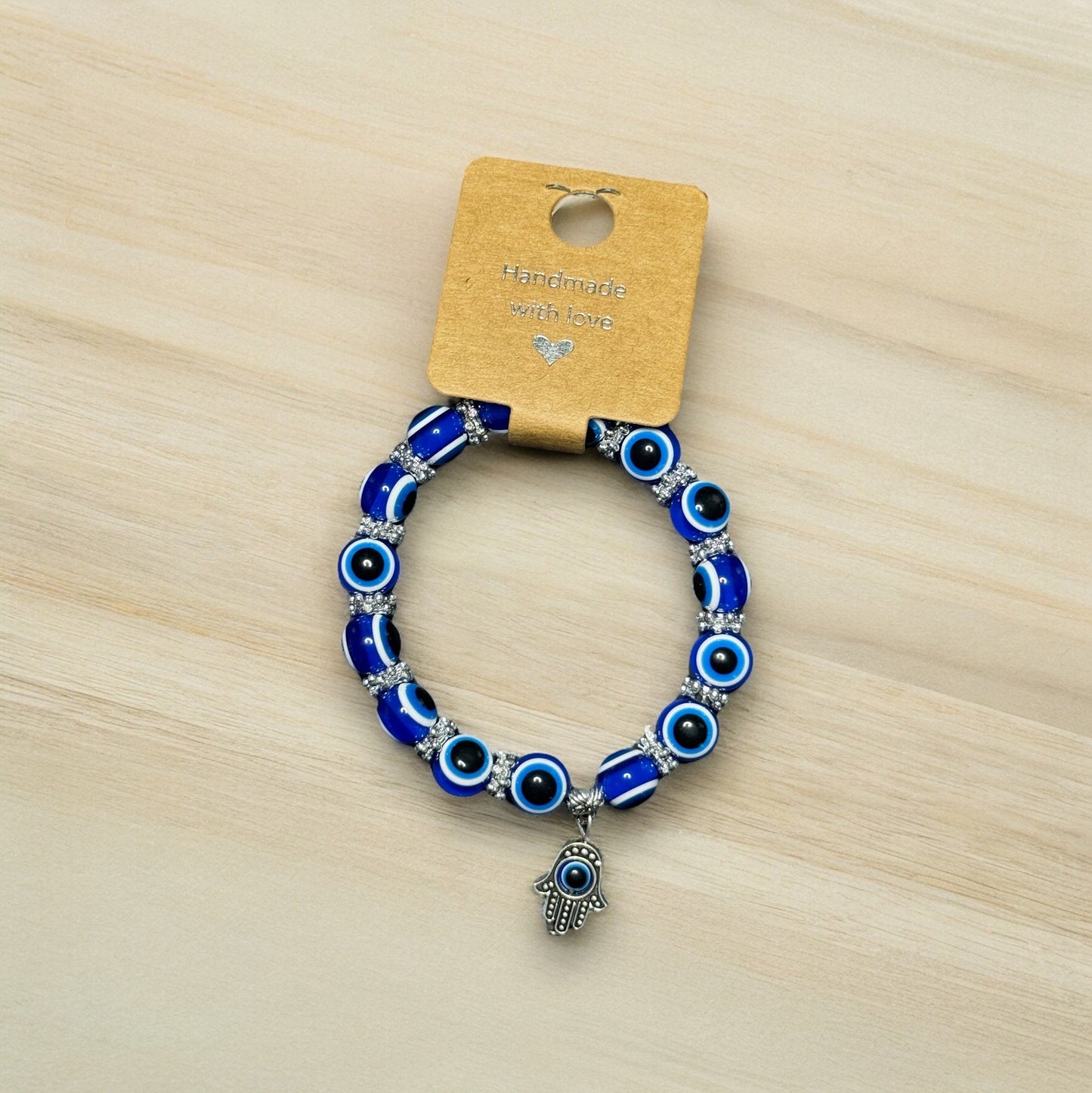 One blue evil eye beaded Hamsa hand bracelet laying on a wooden surface.