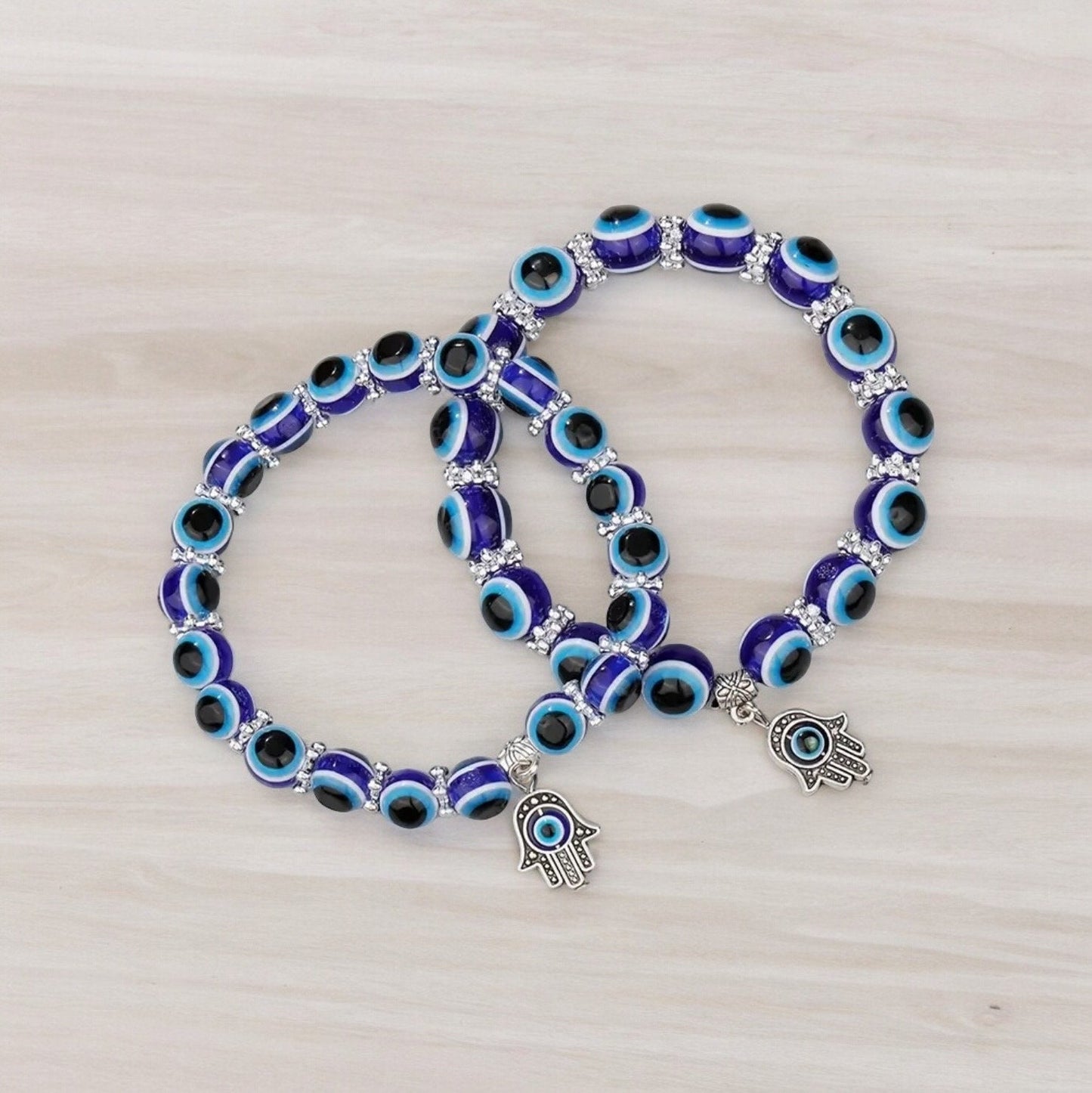 Two blue beaded evil eye bracelets stacked on top of eachother with hamsa hand charms on them.