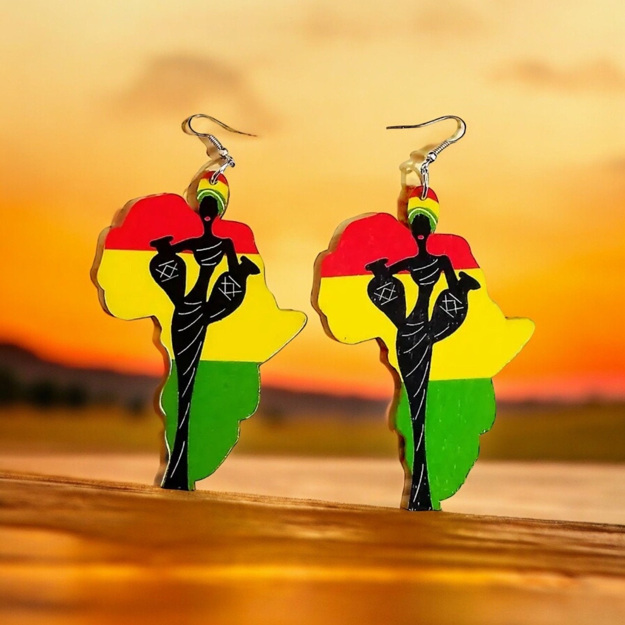 A pair of dangle earrings shaped like the continent of Africa with the Ghana flag print of red, yellow, and green stripes in the background and black silhouette of an African woman holding two vases and wearing a turban on the front.