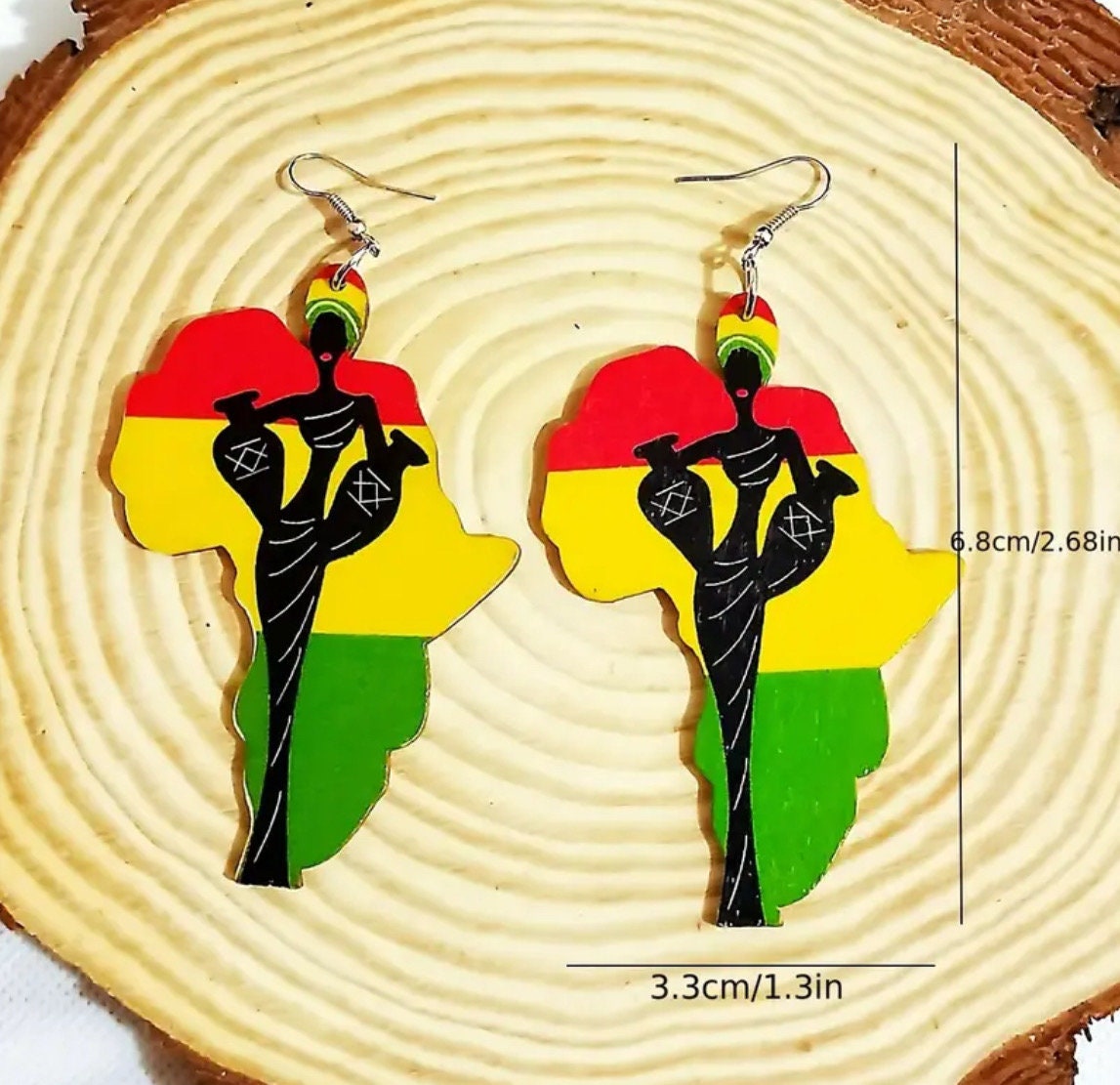 A pair of dangle earrings shaped like the continent of Africa with a red, yellow and green Ghana flag print in the background and the silhouette of an African woman on the front. Dimensions are shown depicting the earrings as being 6.8cm/3.3cm or 2.68in/1.3in in size.