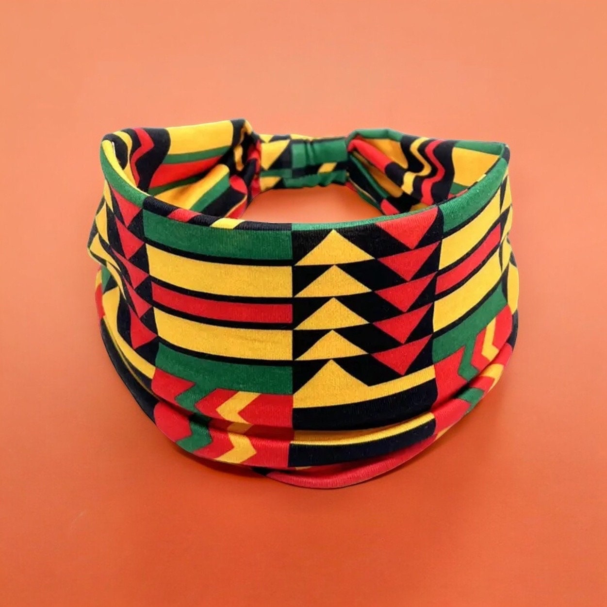 A polyester fabric African print headband that is colored black, yellow, red and green. The print is an artistic, tribal style print with the colors of the Ghana flag.