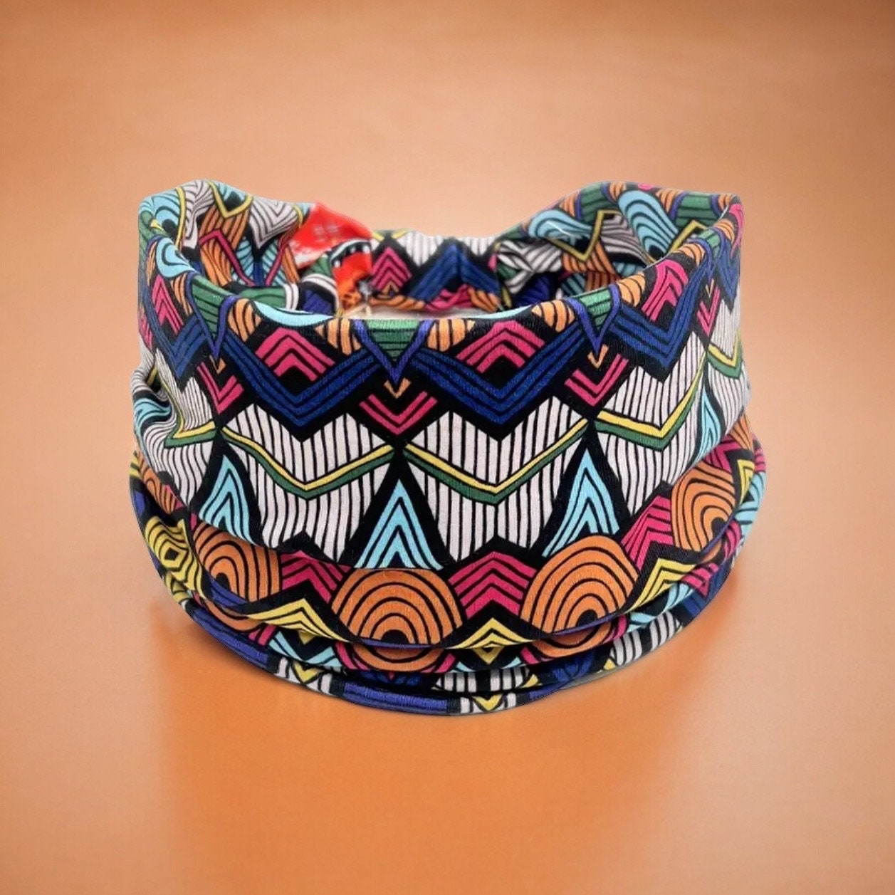 A stretchy polyester headband with an artistic blue tribal print on it. The colors are various shades of blue, orange, yellow, pink, green and white.