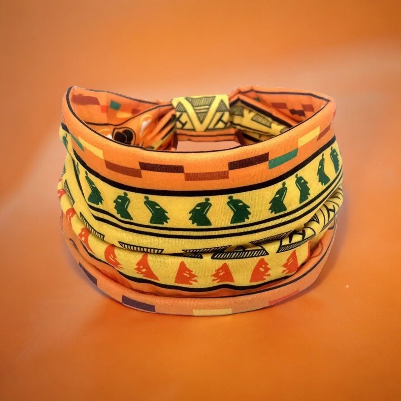 An orange, yellow, green and black African tribal print headband sitting upright.