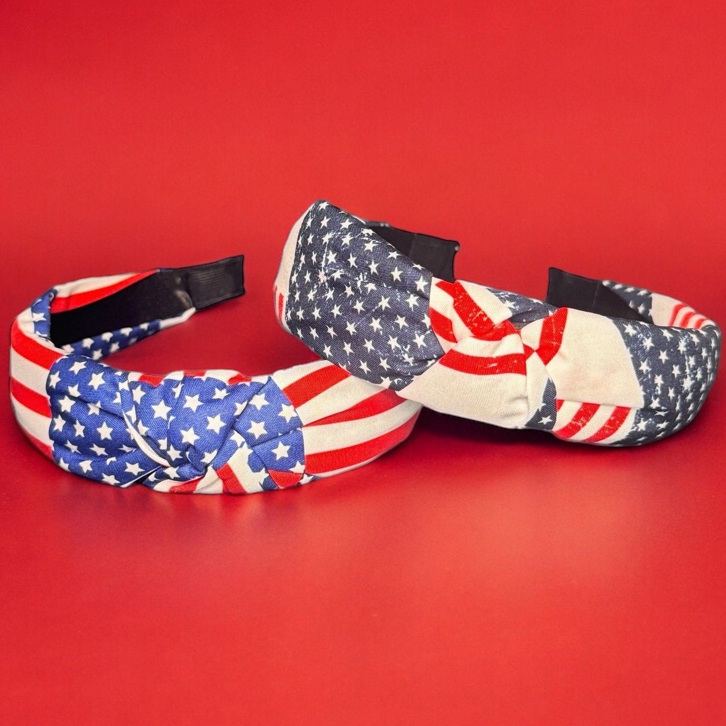 Two wide band fabric knot 4th of July American Flag print headbands laying on a red background.