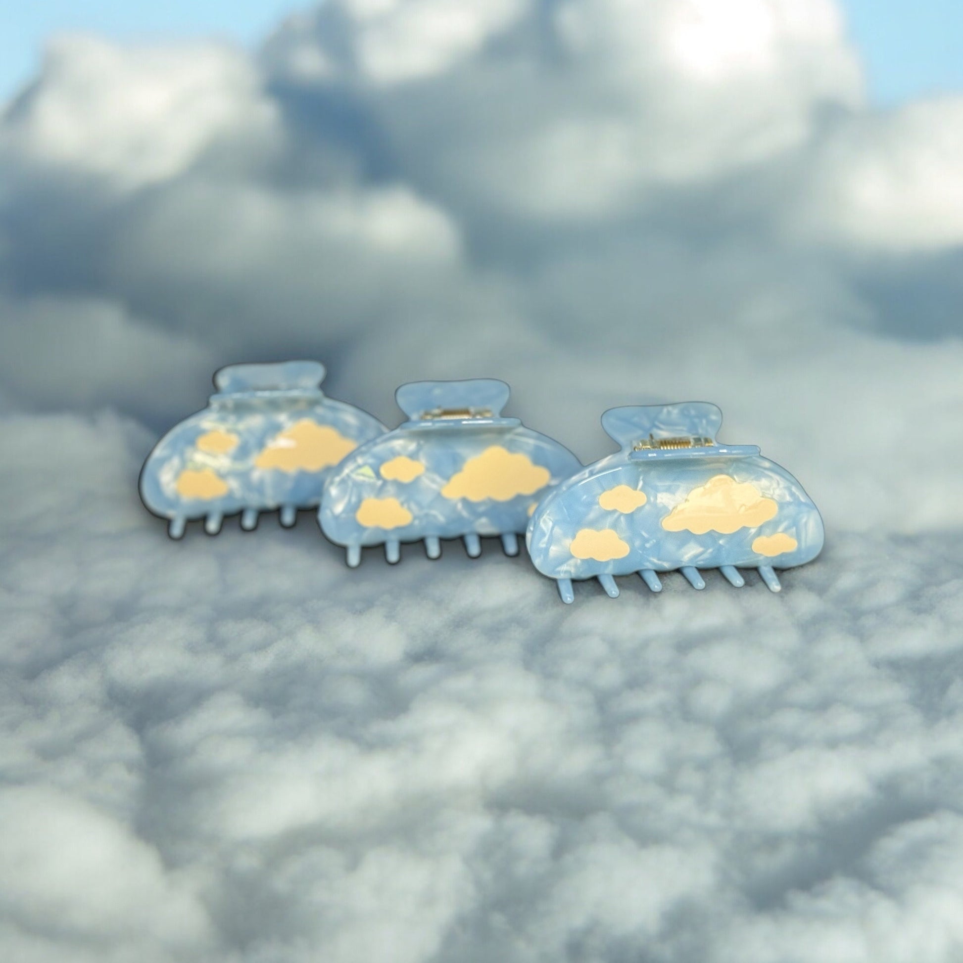 Three light blue colored cloud claw clips standing upright on a fake cloud background.