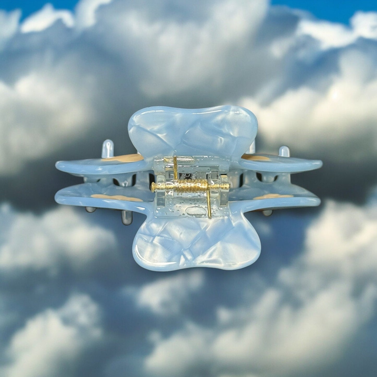 One light blue colored claw clip with white clouds on it from an aerial view showing the top of the clip where the handles and hardware are.