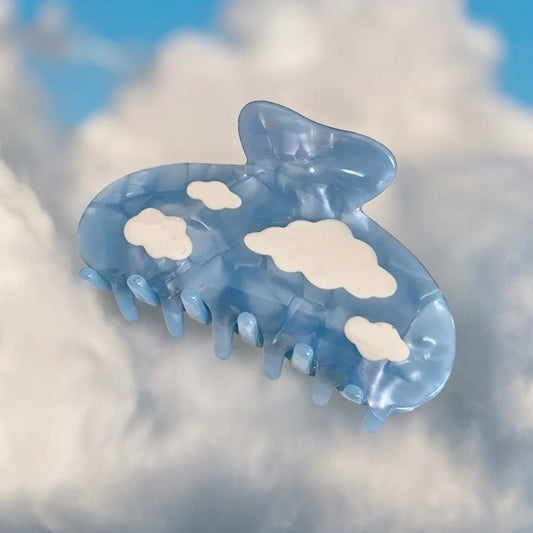 One light blue claw clip with white clouds on it laying down on a surface.