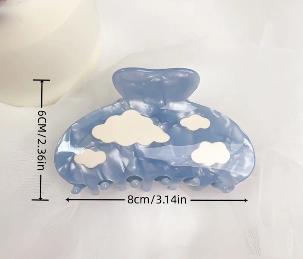 One light blue colored claw clip with white clouds laying on a white background with measurements reading 8x6cm or 3.14x2.36in