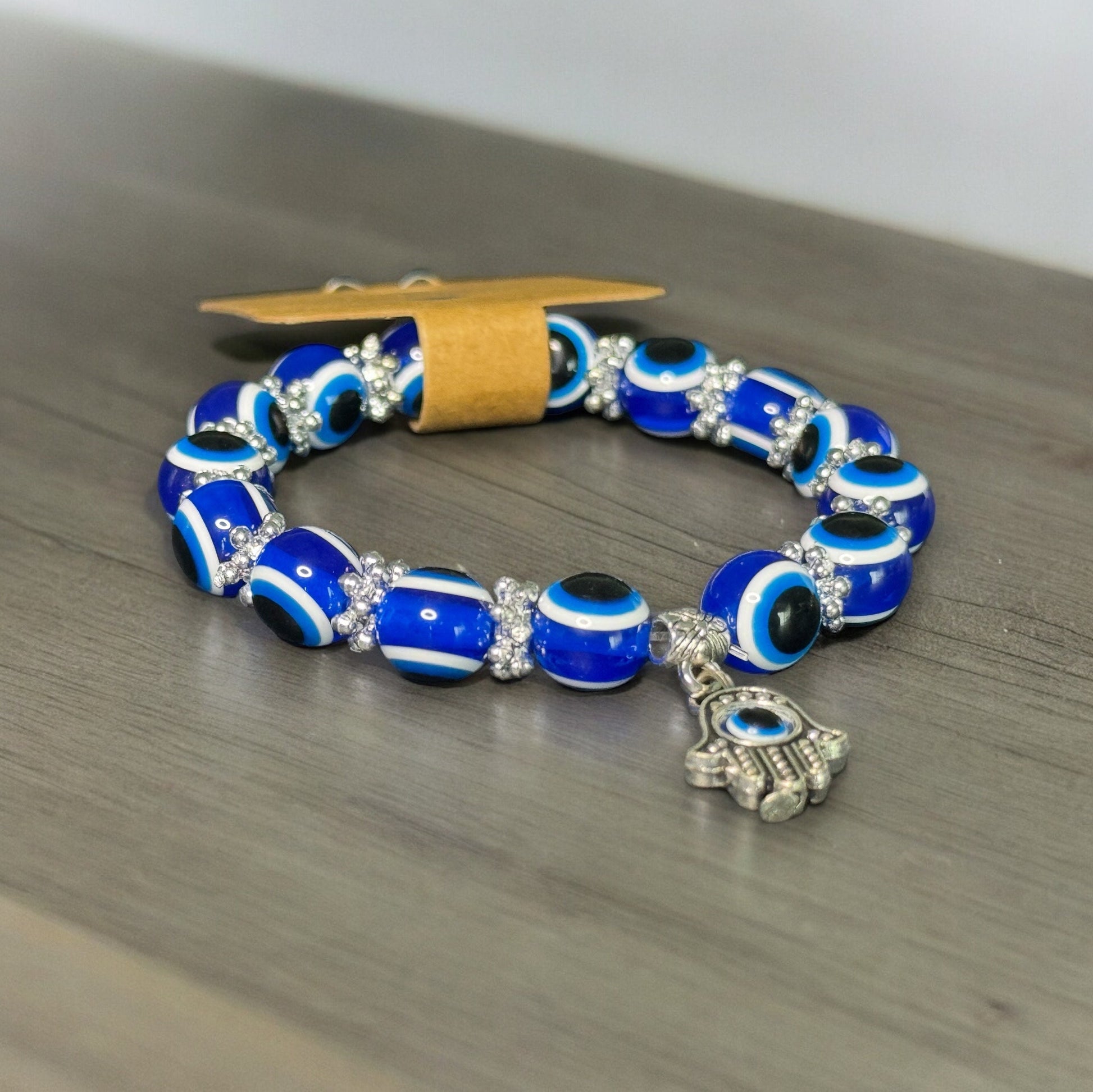 One blue evil eye hamsa hand beaded bracelet laying on a wooden countertop.