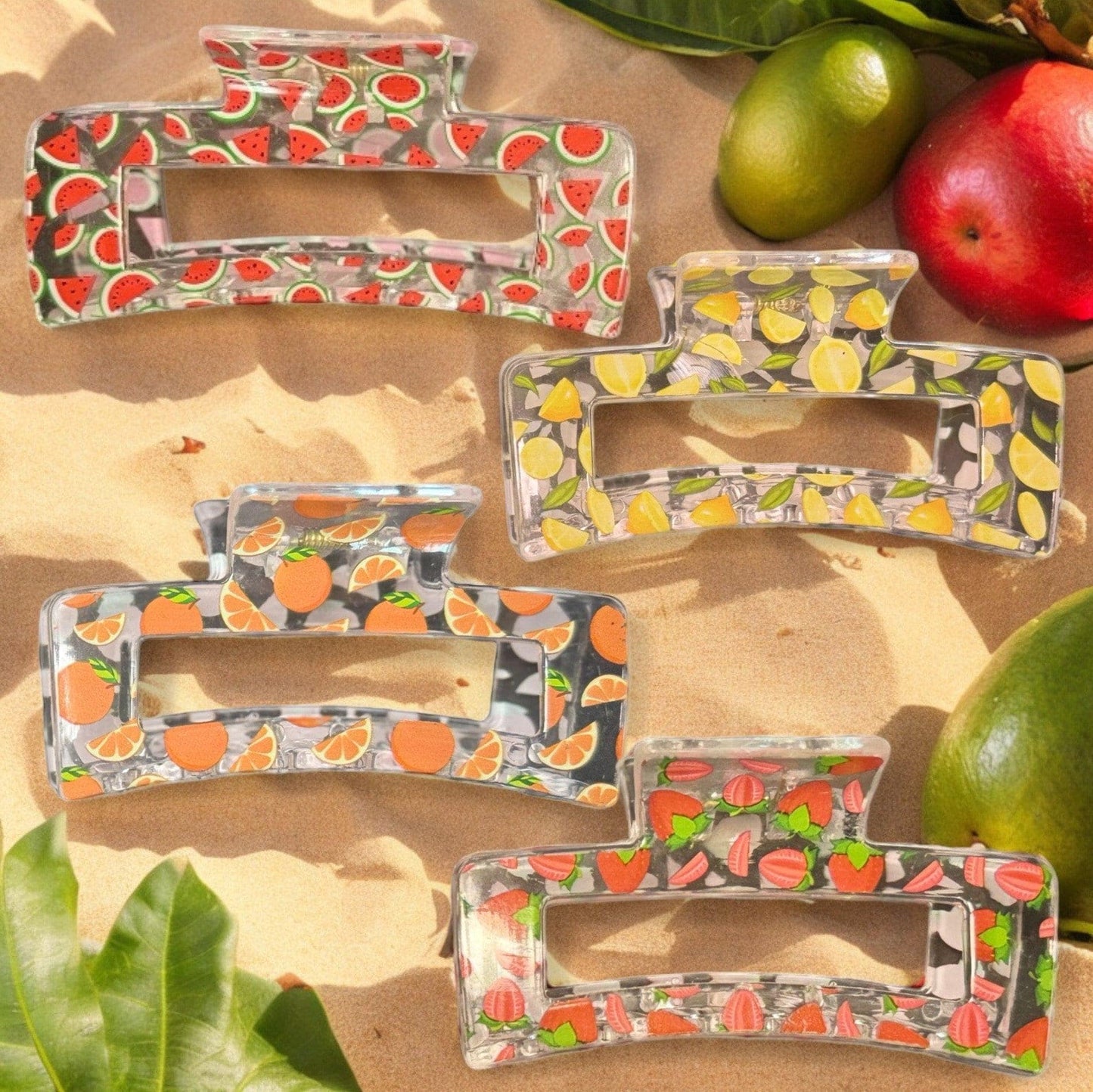 Four clear claw clips with varying fruit prints on them. One has a watermelon print, one has a lemon print, one has an orange print and one has a strawberry print.