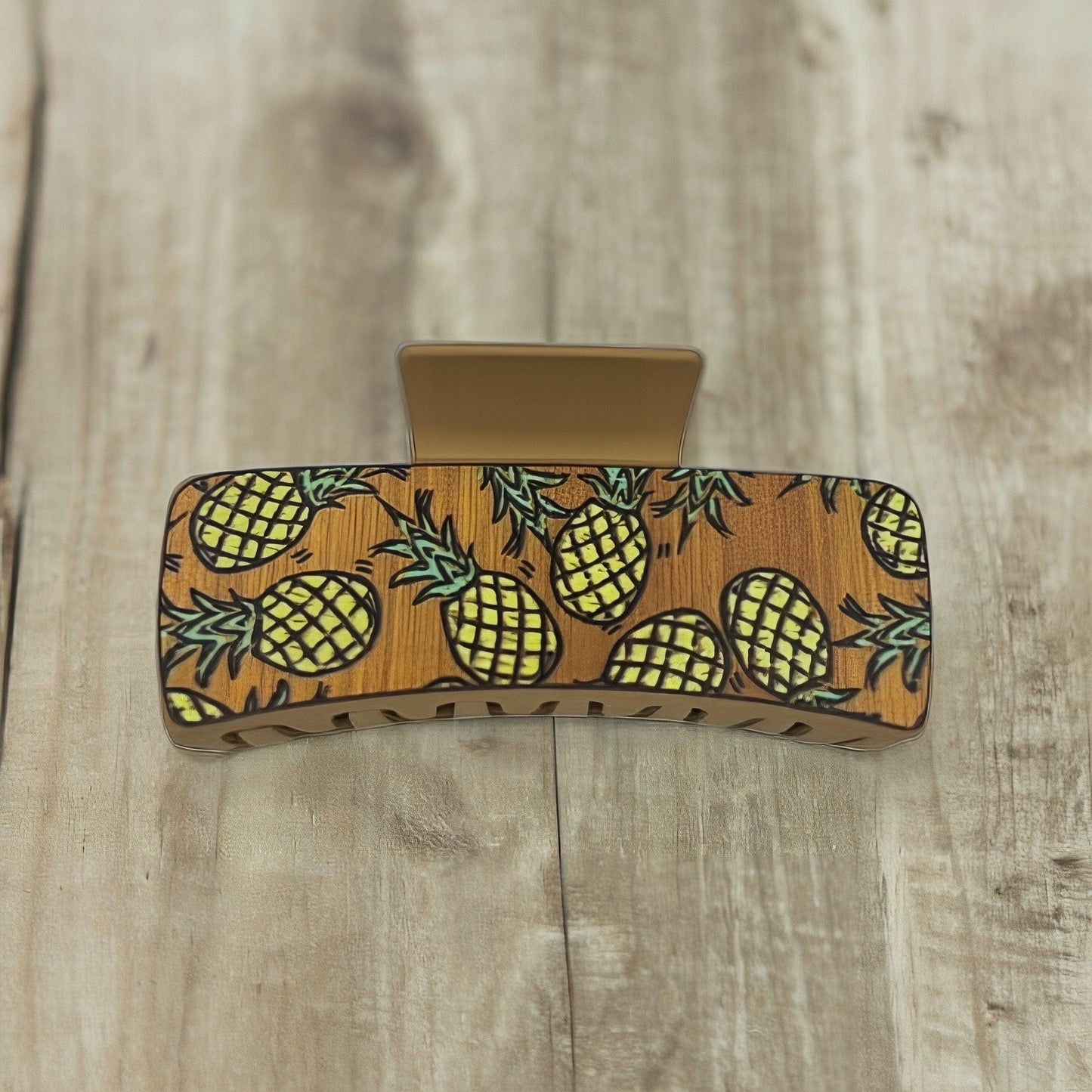 A tan colored medium sized square shaped faux leather claw clip with multiple yellow pineapples on it.