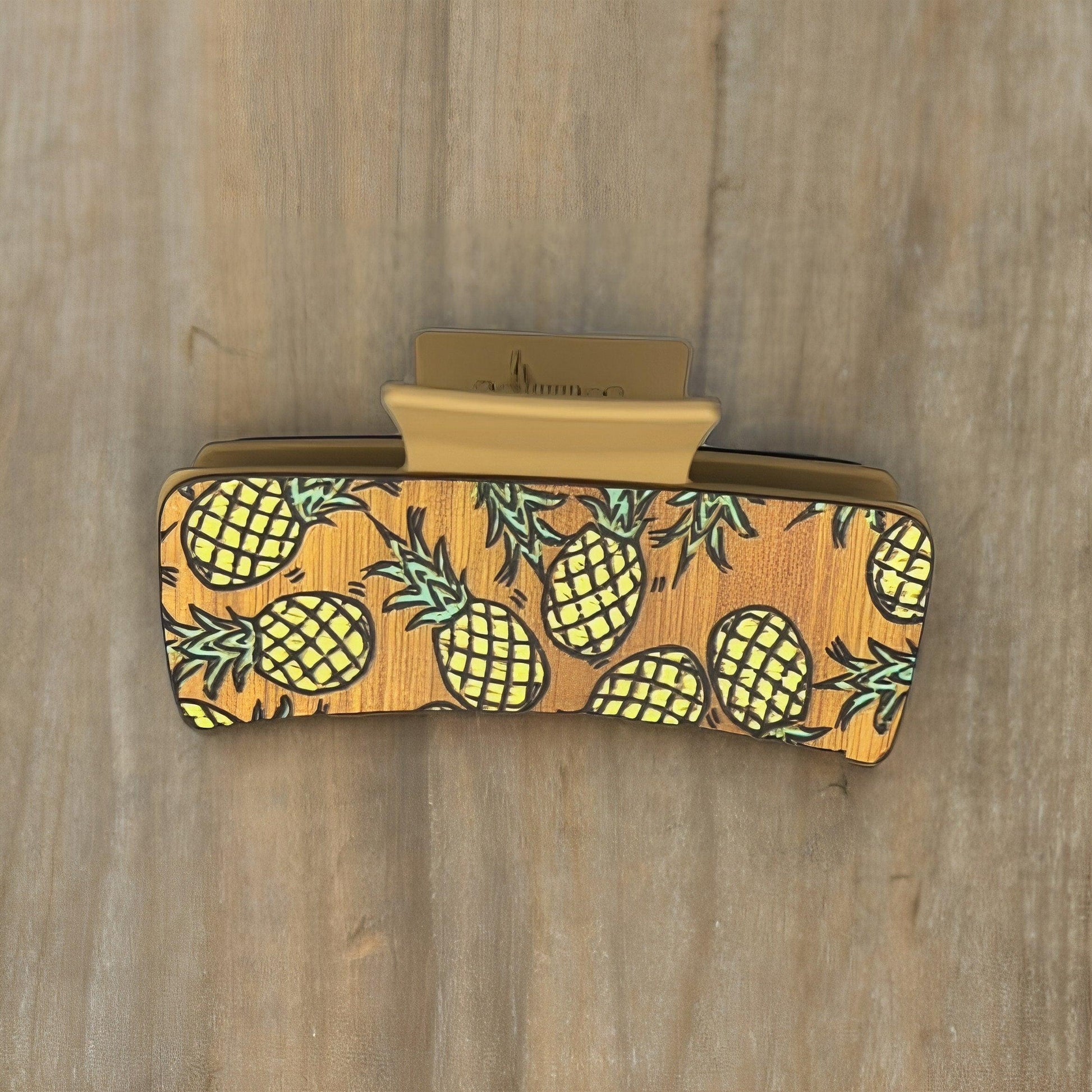 A tan colored medium sized square shaped faux leather claw clip with multiple yellow pineapples on it.