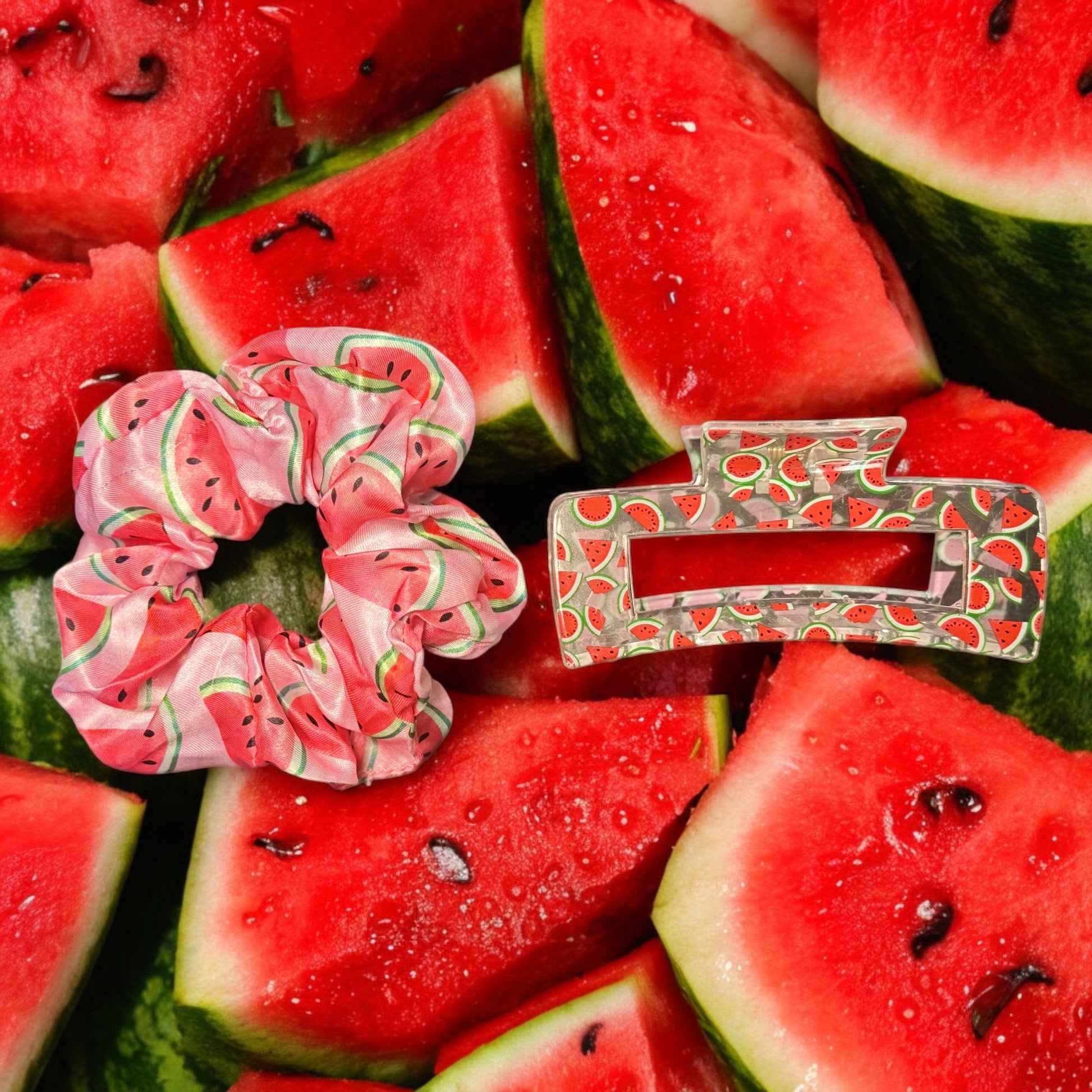 One pink watermelon scrunchie with a clear medium square shaped claw clip with a watermelon print on it on top of a pile of watermelons as the scenery.