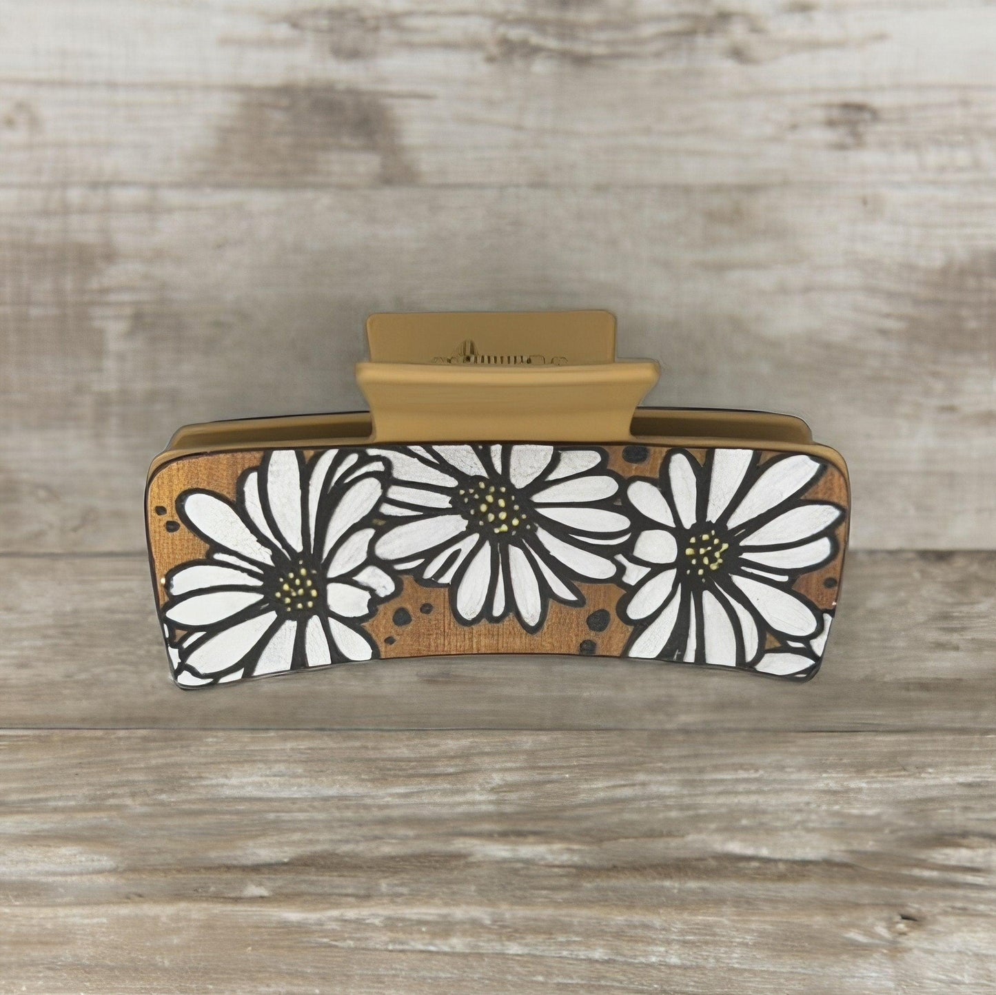 One tan colored medium square shaped faux leather claw clip with multiple white daisies on it.