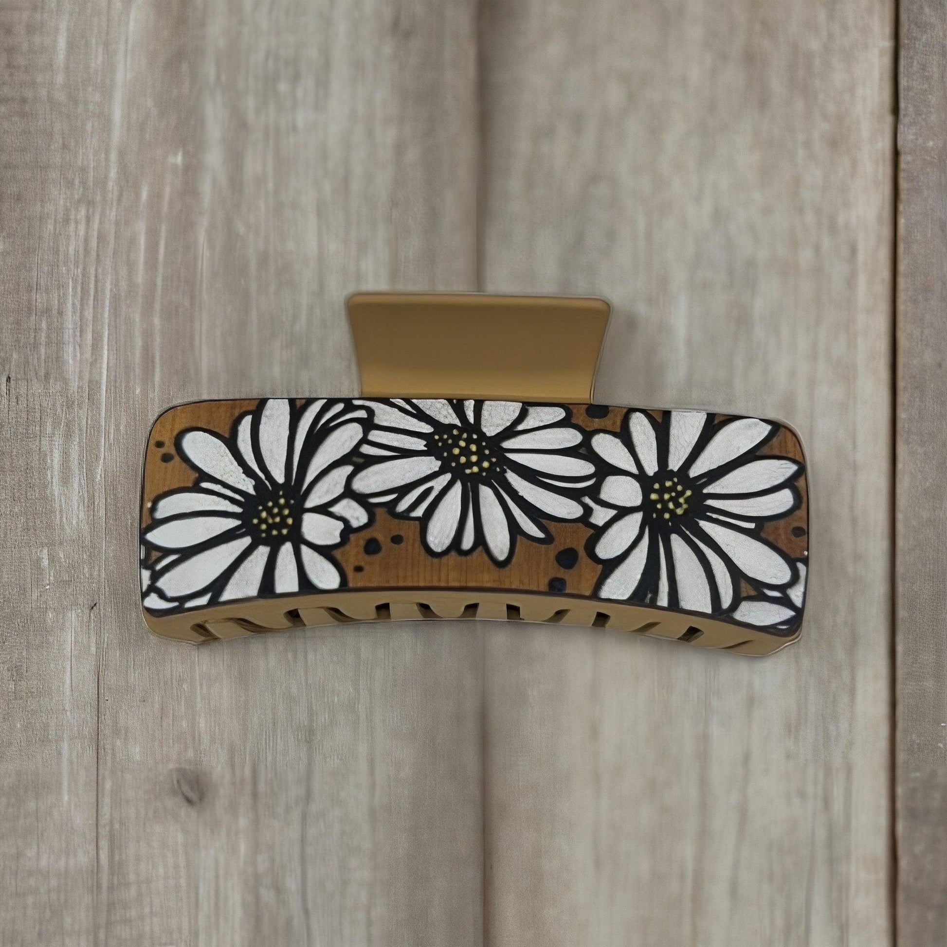 One tan colored medium square shaped faux leather claw clip with multiple white daisies on it.