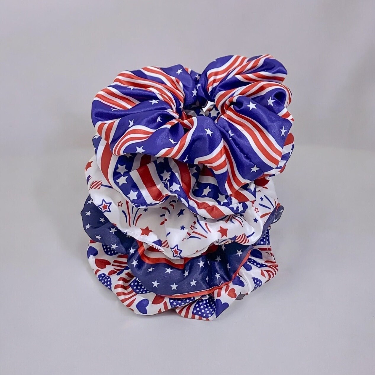 5 scrunchies stacked on top of each other in a vertical pile. Each scrunchie has differing red, white and blue 4th of July themed prints.