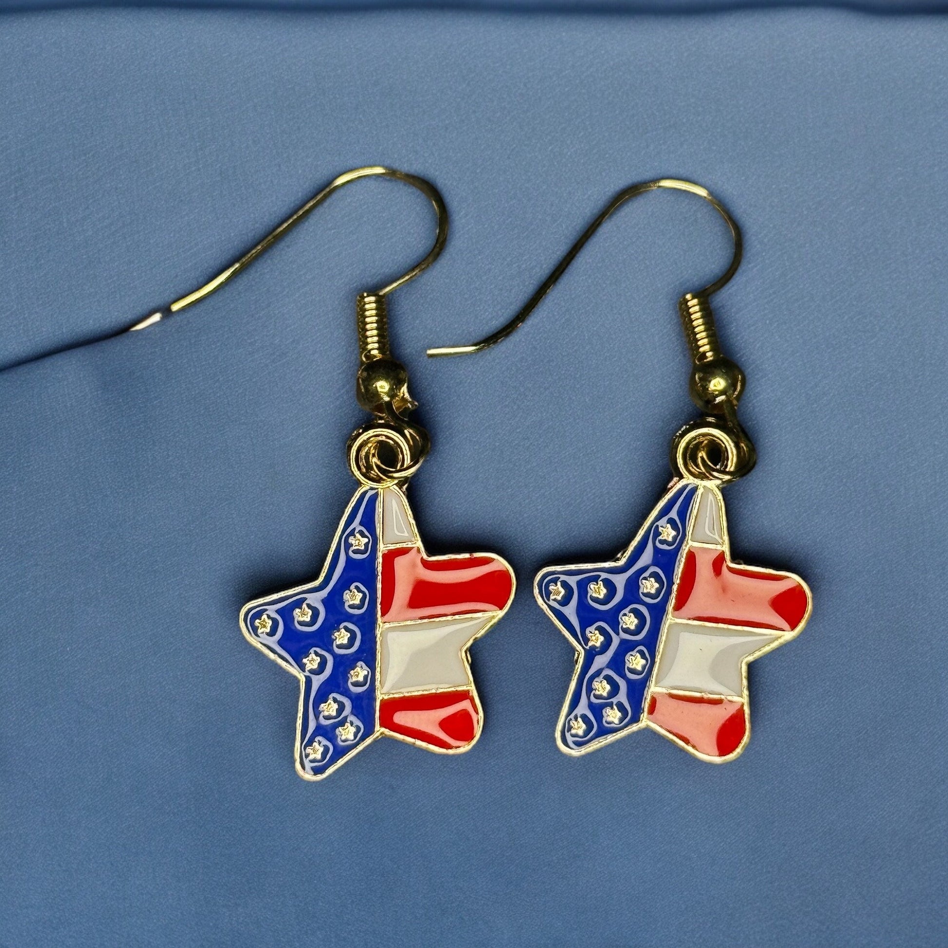 A pair of enamel dangle earrings shaped like stars and colored red, white and blue like the USA flag.